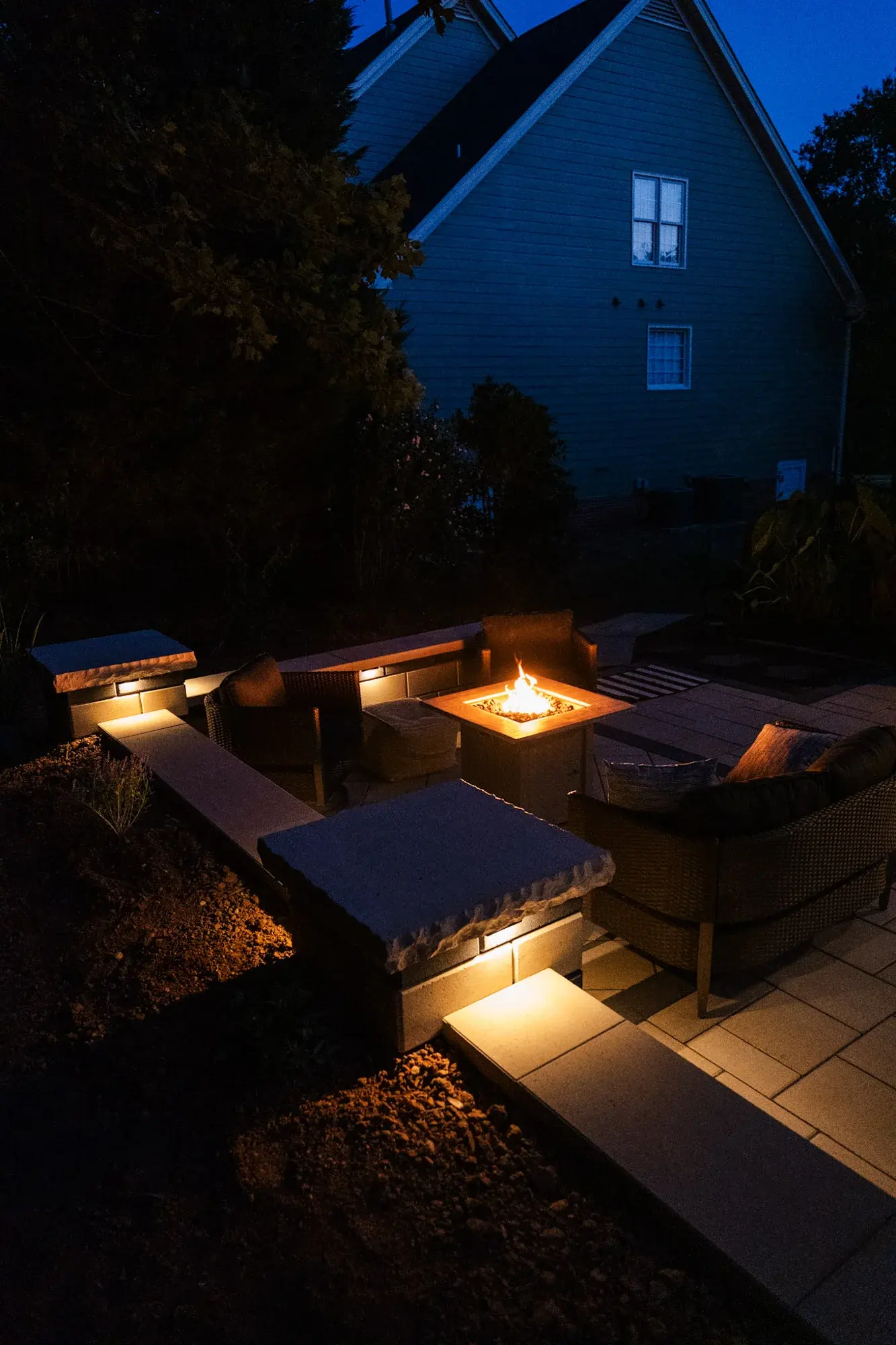 Lit seat wall and fire feature on a backyard patio at night